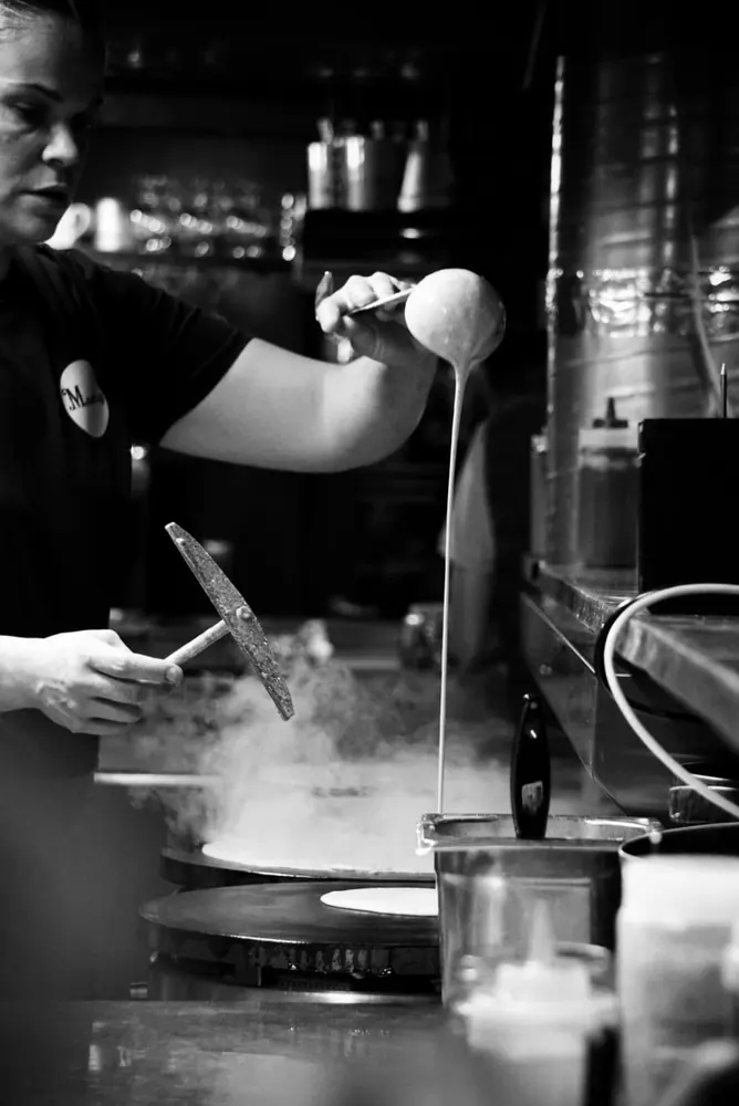 Crêpe maker spreading the batter with a wooden rake on Mamilig’s billig